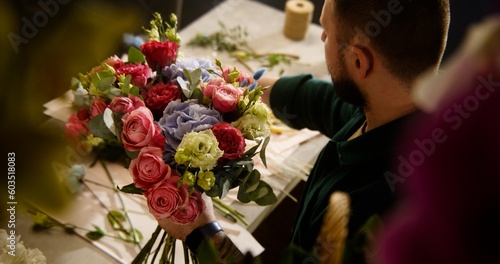 Male professional florist, entrepreneur, seller collects bouquet and makes composition of fresh flowers for customer in flower shop. Concept of floristry, floral small business and entrepreneurship.