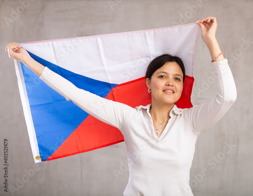 Reliant positive young woman holds big national flag of Czechia with confident smile showing teeth.Labor emigration,study abroad,world without borders.Gray background studio shot photo