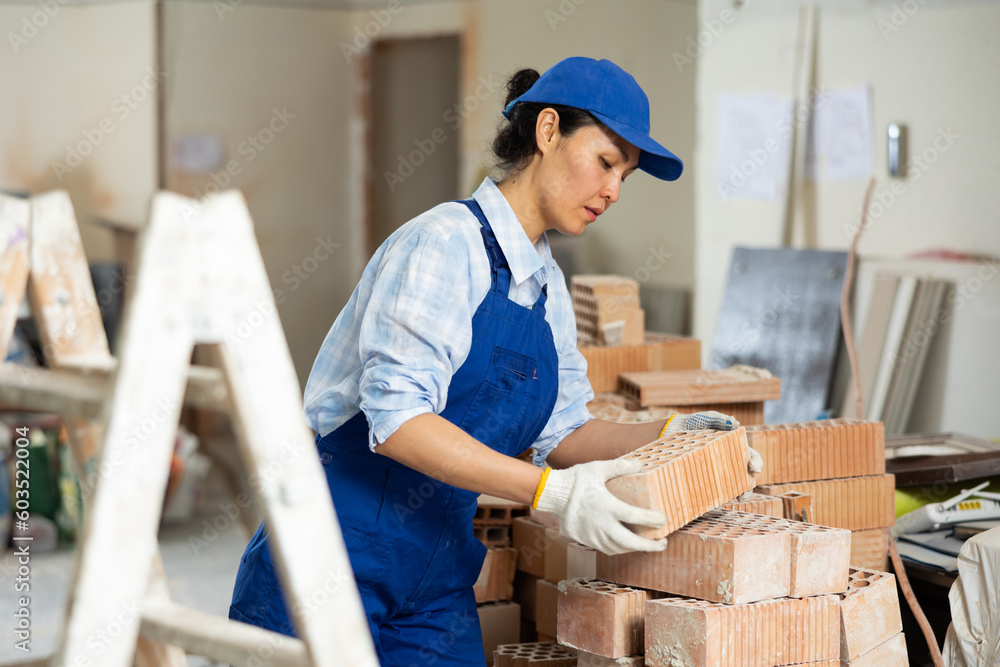 Qualified female builder lays bricks on top of each other, working on a construction site indoors