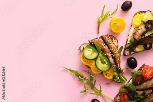 Tasty sandwiches with canned smoked sprats on pink background photo