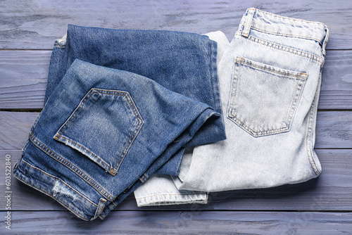 Different stylish denim jeans on blue wooden background