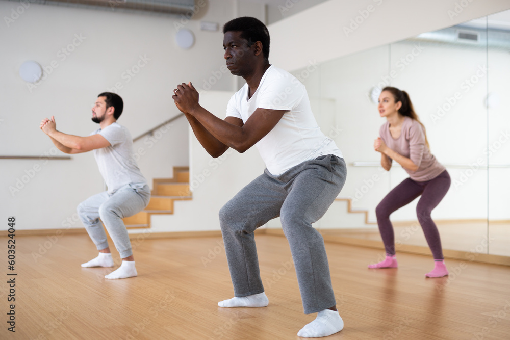 Focused adult African American doing warm up before group yoga class in fitness studio