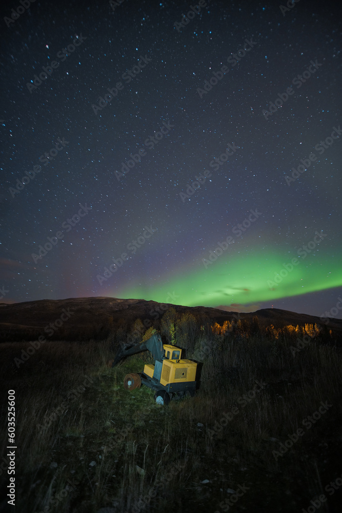 Abandoned heavy machinery excavator at night under northern lights aurora