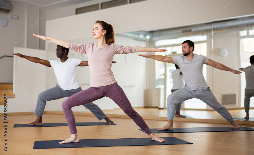 Multiethnic group of people exercising warrior two asana in gym.