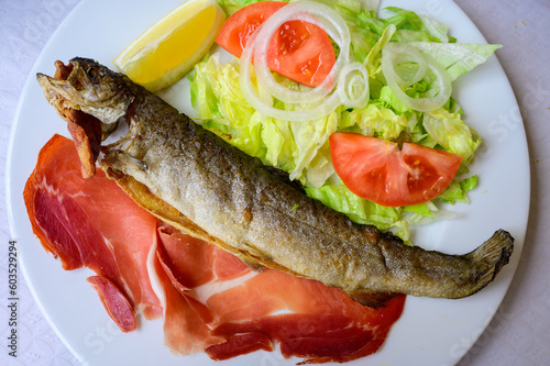Main dish in Asturian restaurant, grilled whole trout fish from mountain river served with fresh mixed salad