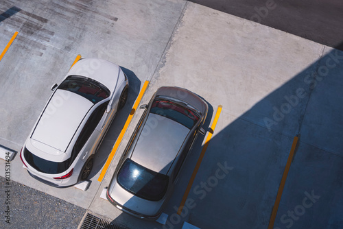 фотографія Top view of 2 cars parked on outdoor parking area in front of building with sunl