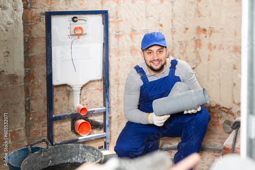 Portrait of plumber in blue overalls holding a plastic sewer pipe in his hands