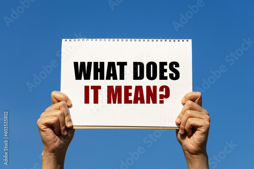 What does it mean text on notebook paper held by 2 hands with isolated blue sky background. This message can be used as business concept about what does it mean.