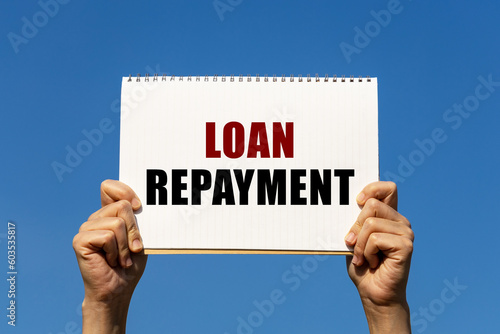 Loan repayment text on notebook paper held by 2 hands with isolated blue sky background. This message can be used as business concept about loan repayment. photo