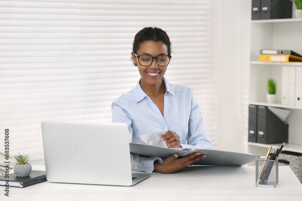 African American intern with folder working at white table in office African American intern with folder working at white table in office