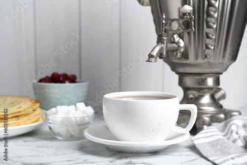 Metal samovar with cup of tea and treats on white marble table, space for text