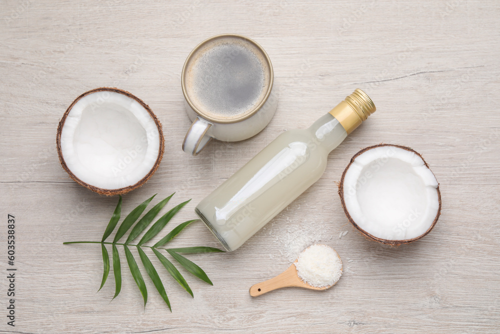 Bottle of delicious syrup, halves of coconut, flakes, cup of coffee and green leaves on white wooden table, flat lay Bottle of delicious syrup, halves of coconut, flakes, cup of coffee and green leaves on white wooden table, flat lay