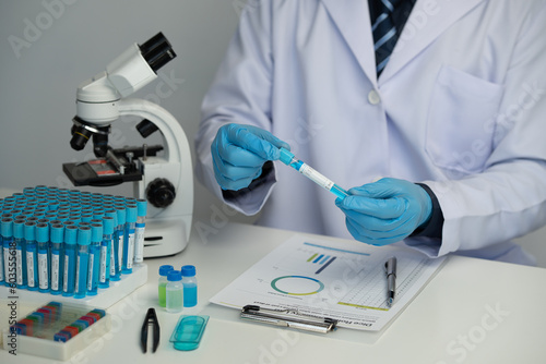 Male scientist using scientific test tubes with data recording of chemicals or drugs tested and examined by microscope in science laboratory for medicine biotechnology biology.