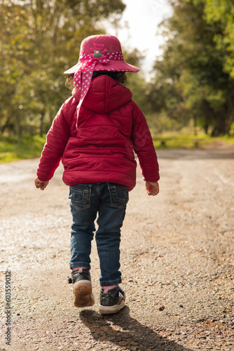 little girl wearing a hat, sweater and jeans pink casual clothes, walking in a sunny day and park nature, childhood lifestyle, portrait