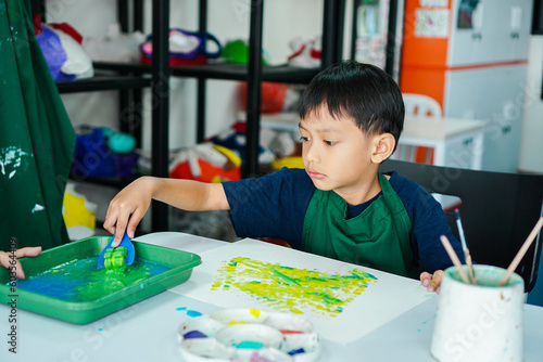 Cute little asian boy kids doing art painting activities in the classroom on the table, Indonesian, Malaysian