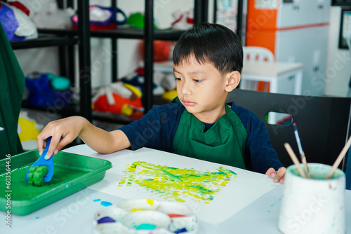 Cute little asian boy kids doing art painting activities in the classroom on the table, Indonesian, Malaysian