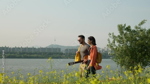 Lovely Happy Couple Dating Outdoors Walking by Han River and Talking Sunset Time at Seorae Island. Flowering Yellow Rapeseed Field in Foreground and Seoul Namsan Tower in Background photo