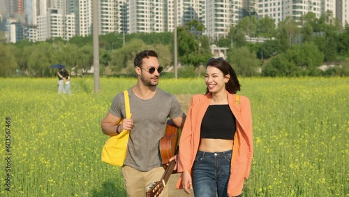 Cheerful Beautiful Couple Walking Through Flowering Canola Meadow Having Lovely Conversation at Seorae Island Hangang Park - Following Tilt up From Legs to Portrait photo