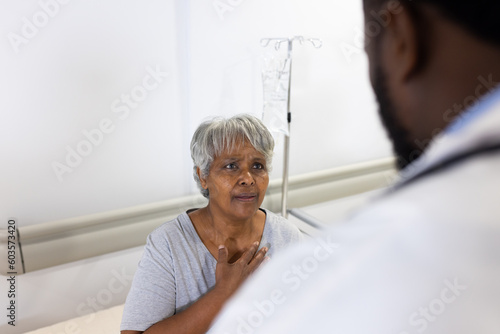 Concerned biracial senior female patient talking to diverse male doctor in hospital, copy space