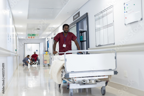 African american male medical worker pushing empty bed in hospital corridor