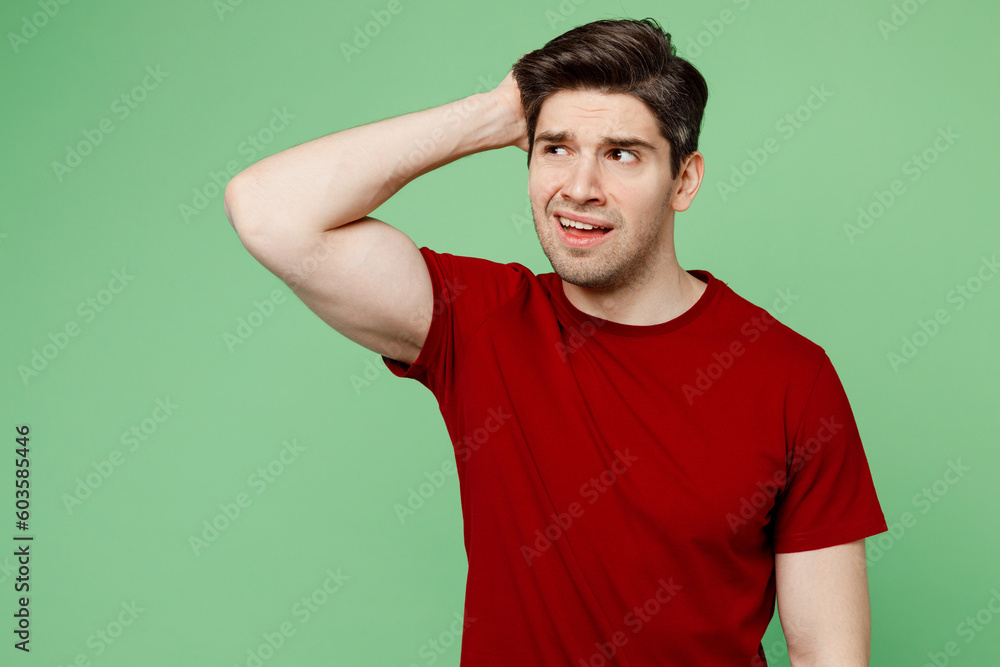 Young sad mistaken puzzled confused brunet caucasian man he wears red t-shirt casual clothes look aside scratch hold head isolated on plain pastel green background studio portrait. Lifestyle concept. Young sad mistaken puzzled confused brunet caucasian man he wears red t-shirt casual clothes look aside scratch hold head isolated on plain pastel green background studio portrait. Lifestyle concept.