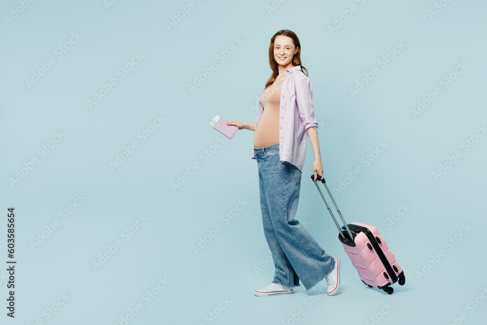 Full body young pregnant mom woman with belly tummy wear casual clothes hold bag passport ticket isolated on plain blue background. Tourist travel abroad in free time rest getaway. Air flight concept. Full body young pregnant mom woman with belly tummy wear casual clothes hold bag passport ticket isolated on plain blue background. Tourist travel abroad in free time rest getaway. Air flight concept.