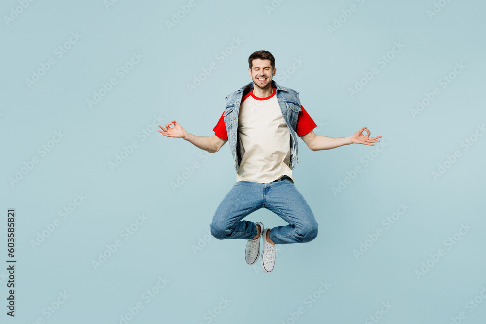 Full body young man wear denim vest red t-shirt casual clothes hold spread hands in yoga om aum gesture relax meditate try calm down isolated on plain pastel light blue background. Lifestyle concept.