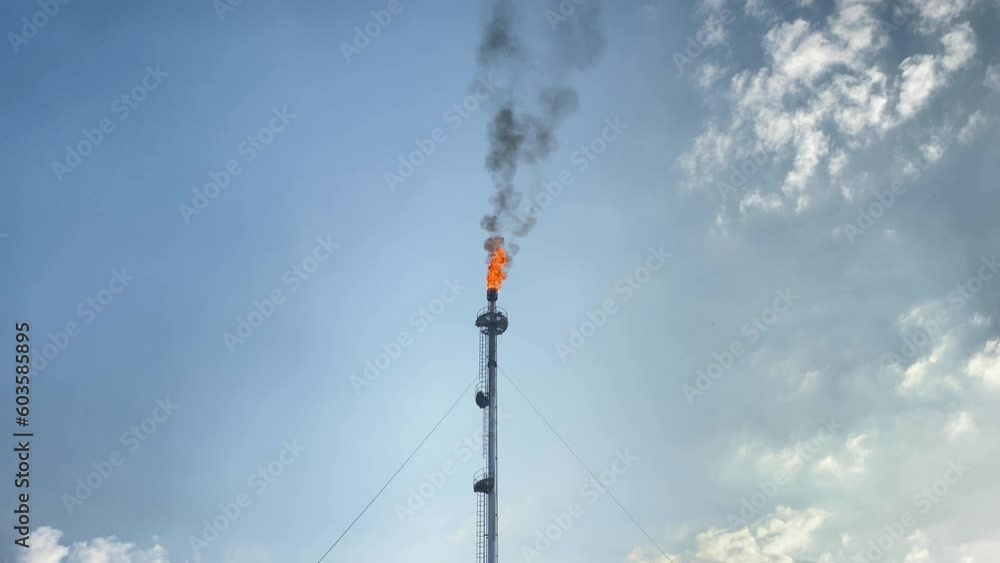 Oil refinery fire stack emits black smoke into blue sky in sunny day Oil refinery fire stack emits black smoke into blue sky in sunny day
