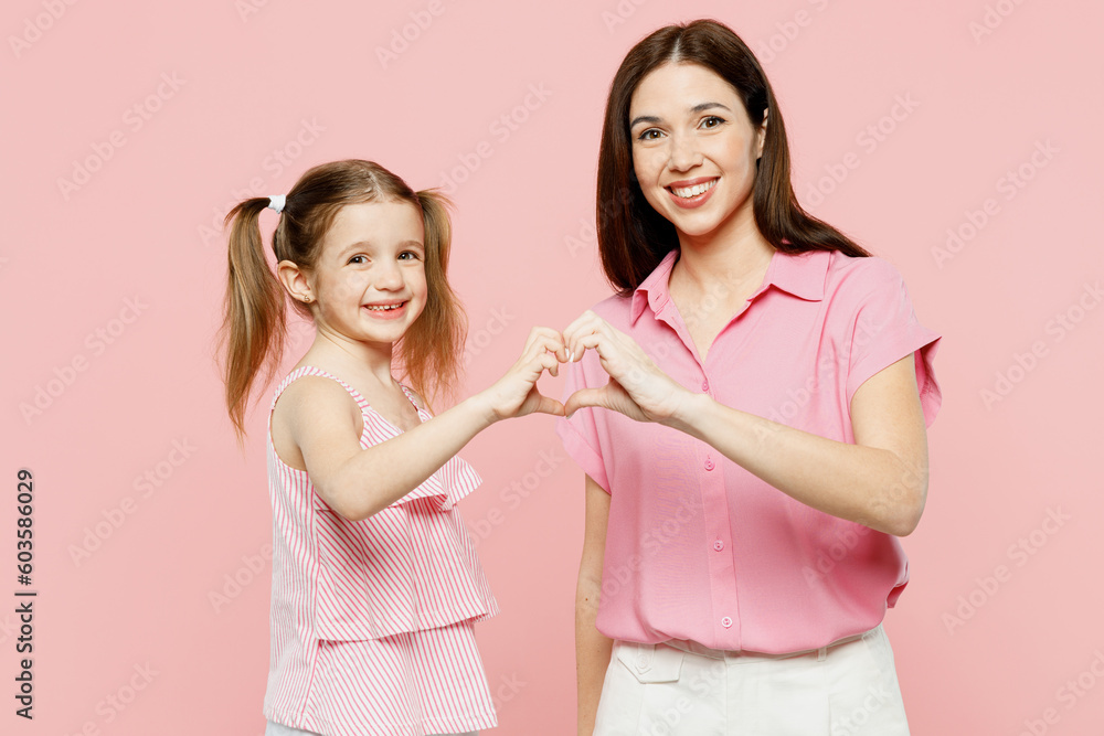 Happy smiling woman wear casual clothes with child kid girl 6-7 years old. Mother daughter show heart shape with hands look camera isolated on plain pastel pink background. Family parent day concept. Happy smiling woman wear casual clothes with child kid girl 6-7 years old. Mother daughter show heart shape with hands look camera isolated on plain pastel pink background. Family parent day concept.