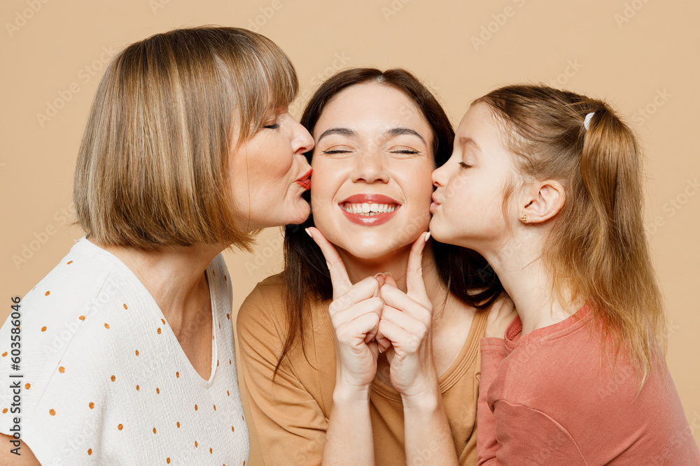 Close up happy lovely women wear casual clothes with kid girl 6-7 years old. Granny mother daughter holding hands kiss mommy close eyes isolated on plain beige background. Family parent day concept. Close up happy lovely women wear casual clothes with kid girl 6-7 years old. Granny mother daughter holding hands kiss mommy close eyes isolated on plain beige background. Family parent day concept.