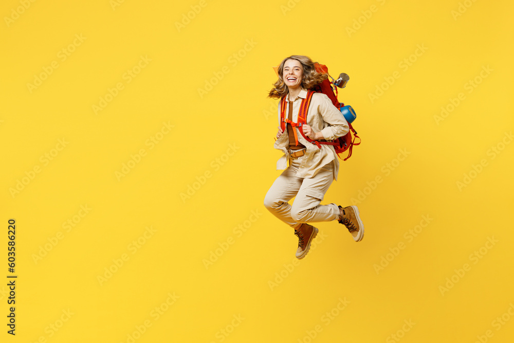 Full body sideways smiling young woman carry bag with stuff mat jump high isolated on plain yellow background. Tourist leads active lifestyle walk on spare time. Hiking trek rest travel trip concept.