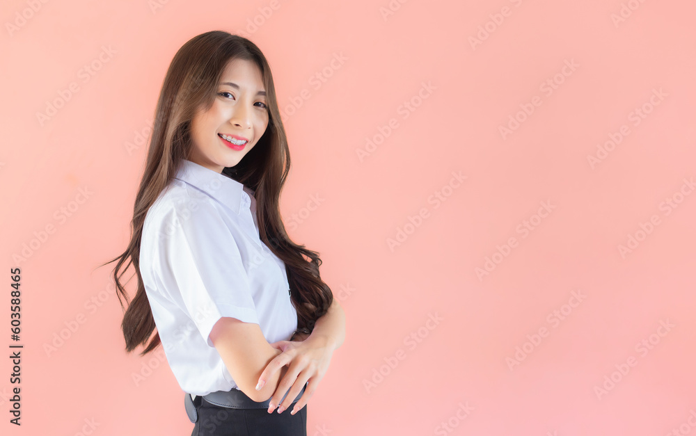Portrait of young Thai student in university student uniform. Asian cute girl standing with her arms crossed confidently isolated on peach color background. Portrait of young Thai student in university student uniform. Asian cute girl standing with her arms crossed confidently isolated on peach color background.