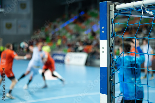 Detail of handball goal post with net and players in the background.