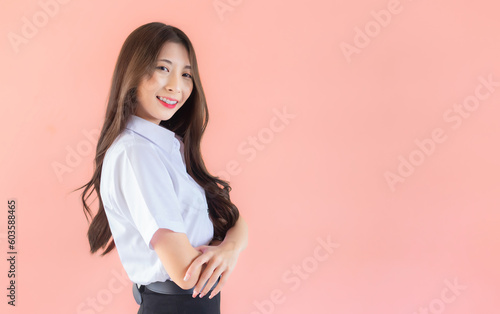 Portrait of young Thai student in university student uniform. Asian cute girl standing with her arms crossed confidently isolated on peach color background.
