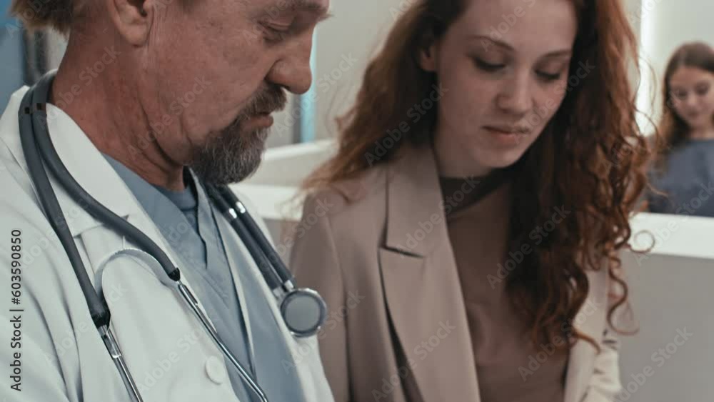 Tilt up shot of mature Caucasian practitioner and his young patient standing in hospital lobby discussing diagnostic test results Tilt up shot of mature Caucasian practitioner and his young patient standing in hospital lobby discussing diagnostic test results