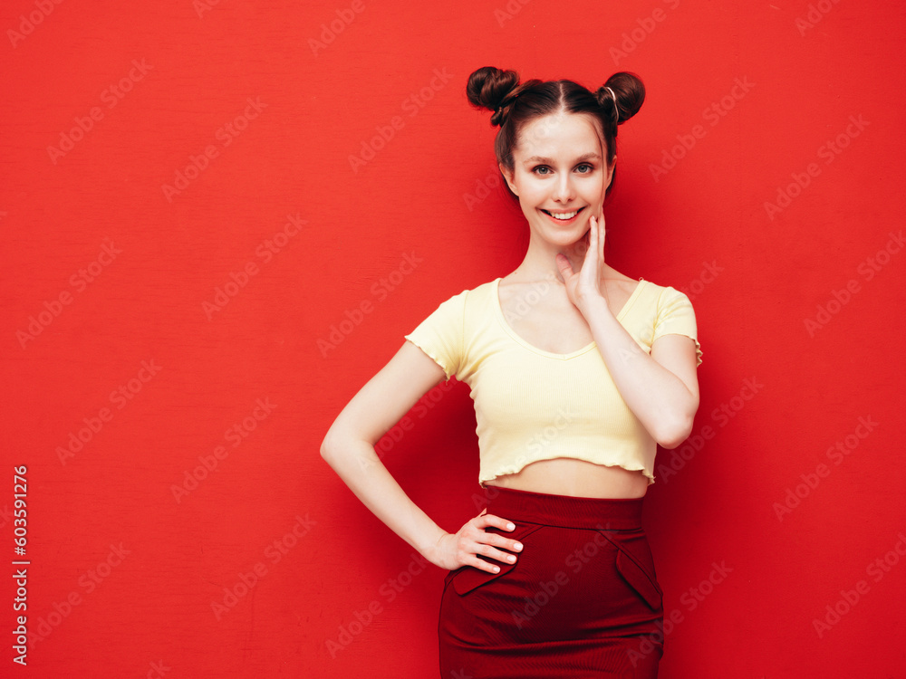 Young beautiful smiling female in trendy summer yellow t-shirt and skirt. Carefree woman with two horns hairstyle posing near red wall in studio. Positive model having fun. Cheerful and happy Young beautiful smiling female in trendy summer yellow t-shirt and skirt. Carefree woman with two horns hairstyle posing near red wall in studio. Positive model having fun. Cheerful and happy