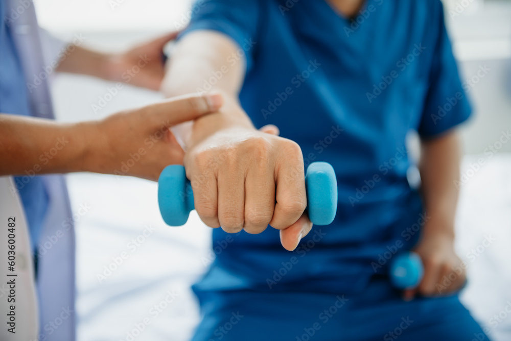 Asian physiotherapist helping male patient stretching arm during exercise correct with dumbbell in hand during training hand  in hospital