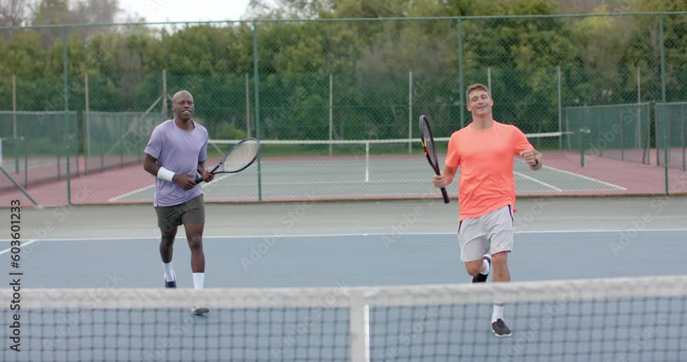 Two diverse male friends playing doubles celebrating winning point on outdoor court in slow motion Two diverse male friends playing doubles celebrating winning point on outdoor court in slow motion