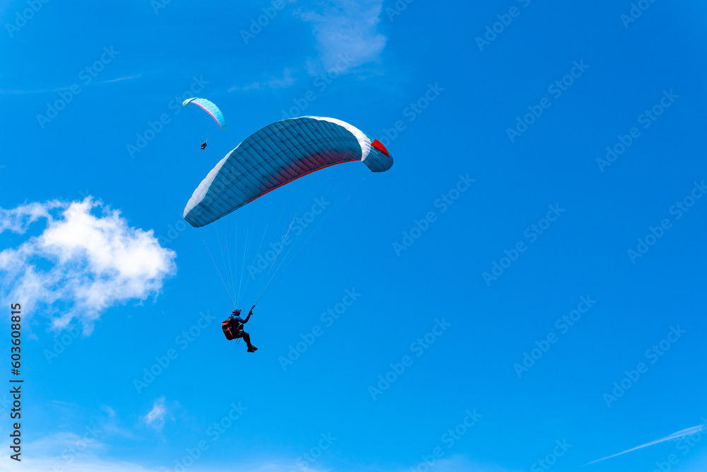 Paragliders fly in the blue sky against the background of clouds. Paragliding in the sky on a sunny day. Paragliders fly in the blue sky against the background of clouds. Paragliding in the sky on a sunny day.