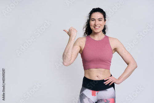Beautiful female athlete smiling looking at camera, pointing aside at copy space on white background