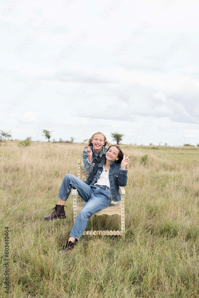 Smiling girl friends sitting in chair in field Smiling girl friends sitting in chair in field
