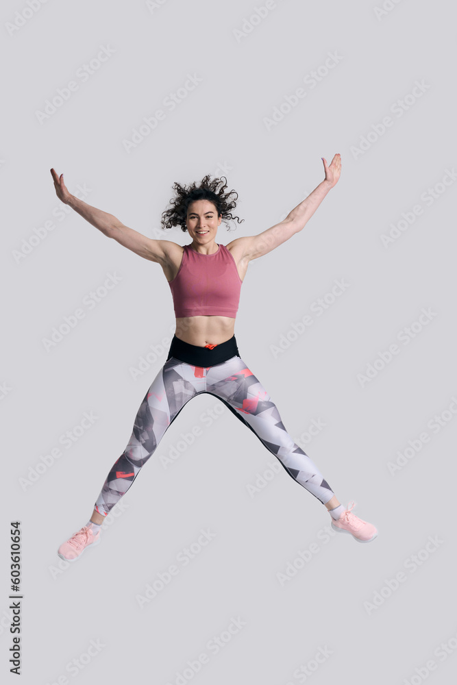 Athlete woman wearing stylish sports suit sneakers, jumps high up over white background. Full length