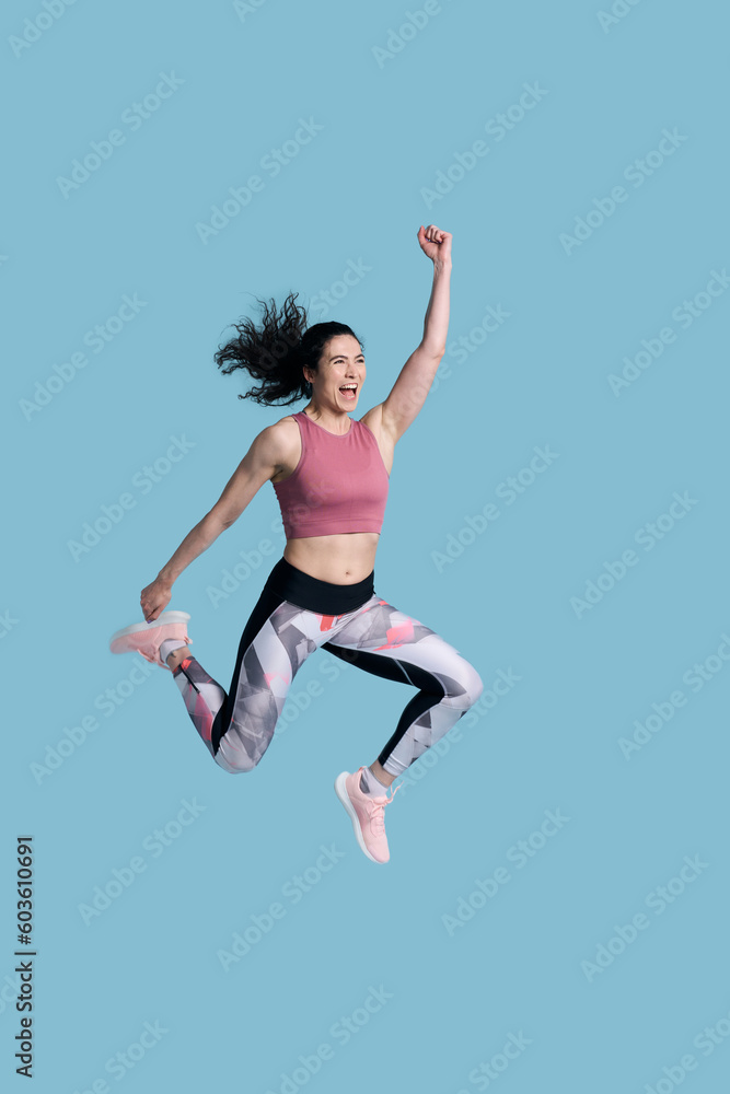 Cheerful determined female athlete in sportswear, smiling and jumping high on blue background Cheerful determined female athlete in sportswear, smiling and jumping high on blue background