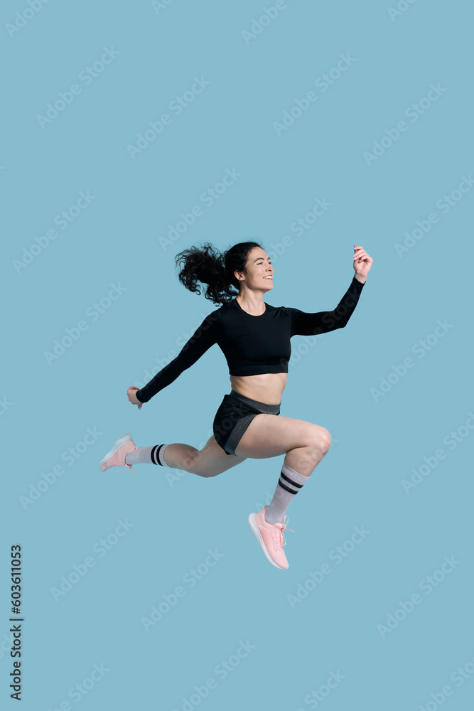 Full length side studio portrait of a sportswoman, running fast over blue background. Sport. Fitness
