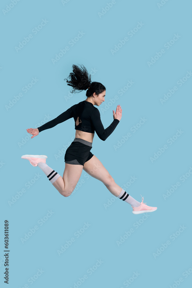 Side portrait athlete woman in black sportswear runs over blue background. People. Sport. Endurance