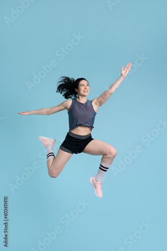 Determined, competitive sportswoman, jumping high up, stretching, exercising over blue background