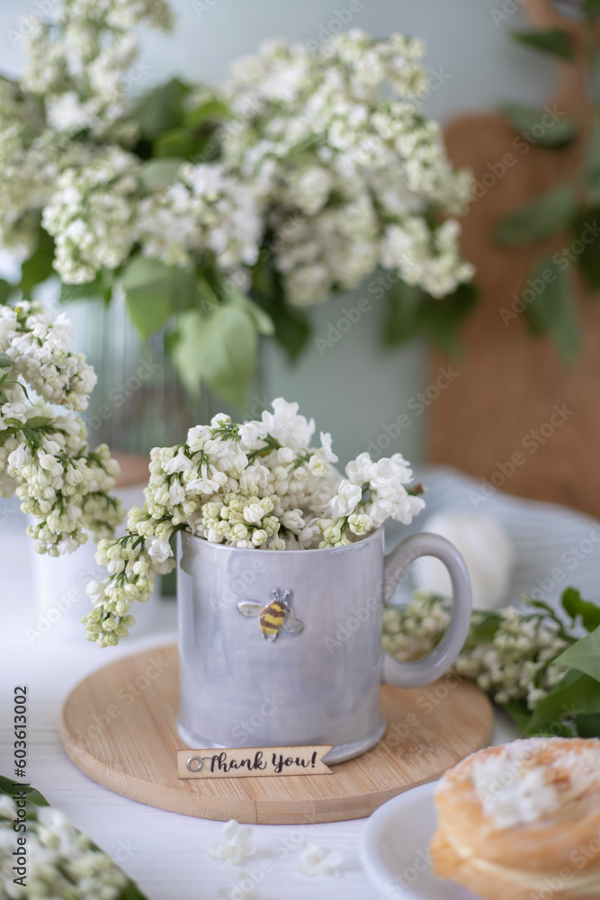 A gray cup with the image of a bee, white lilac flowers and a cake. Tea party with flowers A gray cup with the image of a bee, white lilac flowers and a cake. Tea party with flowers