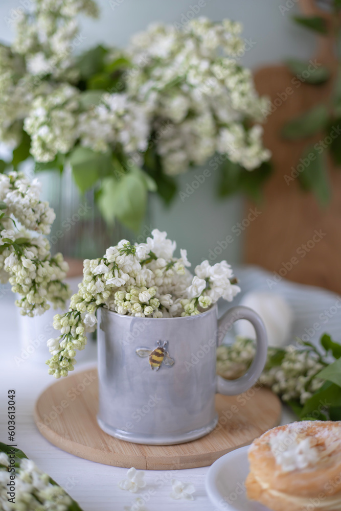A gray cup with the image of a bee, white lilac flowers and a cake. Tea party with flowers