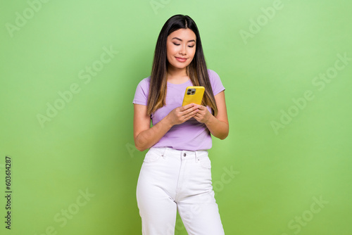 Photo of young charming japanese woman wear violet t-shirt hold smartphone text her friends online chat isolated on green color background