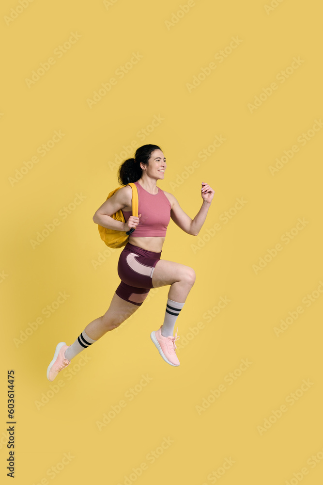 Female jogger with yellow backpack, jogging marathon, fast running, speed race on yellow background
